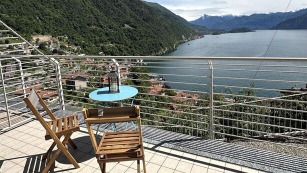 A balcony with a table and chairs overlooking a lake and mountains.