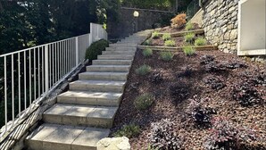 A staircase leading up to a house with a stone wall and a metal railing.