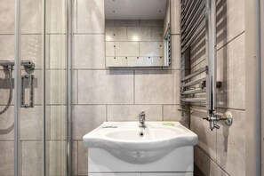 Enjoy a refreshing shower in the bathroom, featuring a glass-enclosed shower area with handheld showerhead and pedestal sink.