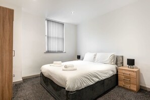 Relax in a serene bedroom with a large bed, neutral-toned bedding, and a wooden nightstand.