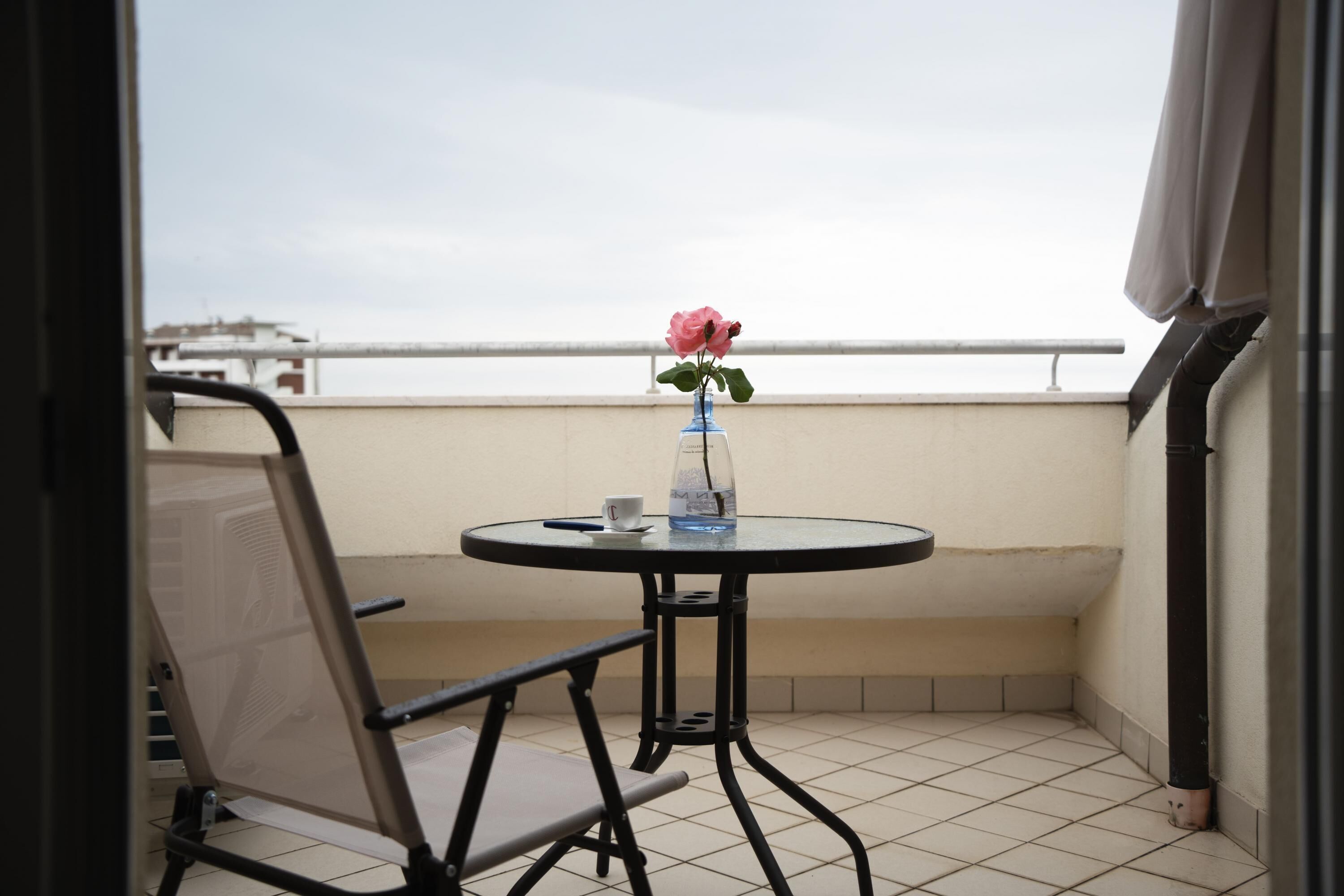 A small balcony with a round table, a chair, a vase with a single flower, and a cup.
