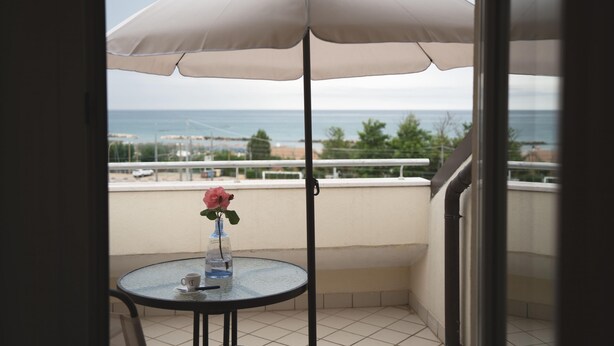 A balcony with a round table, a white umbrella, and a vase with a pink flower. - Cucci House Lido Riccio (Ortona)