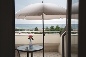 A balcony with a round table, a white umbrella, and a vase with a pink flower.