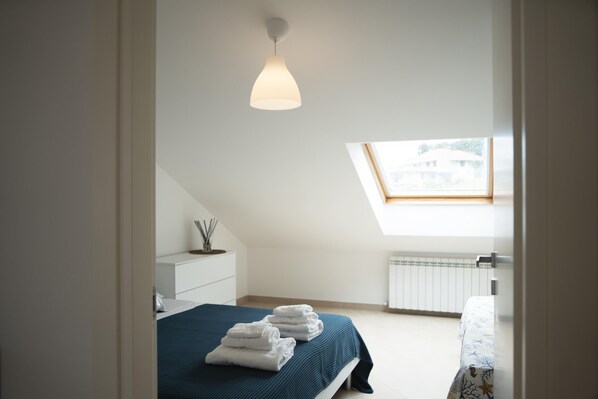 A bedroom with a skylight, a bed with a blue bedspread, and a bedside table with a lamp.