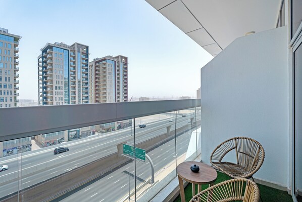 A balcony with a view of a highway and tall buildings. There are two wicker chairs and a small table.
