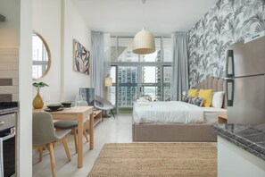 Habitación de hotel moderna con una cama grande, un área de comedor, una cocina y vistas a la ciudad.