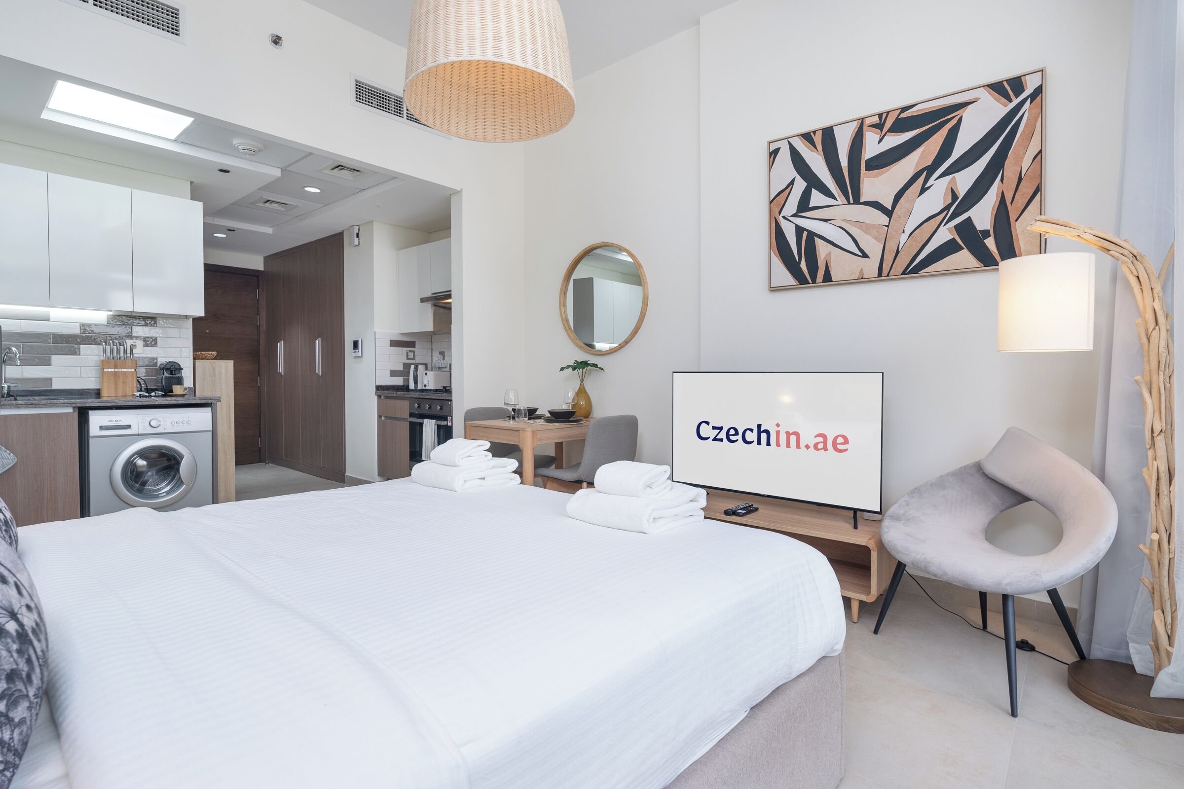 A hotel room with a bed, a desk, a chair, a TV, and a washing machine.