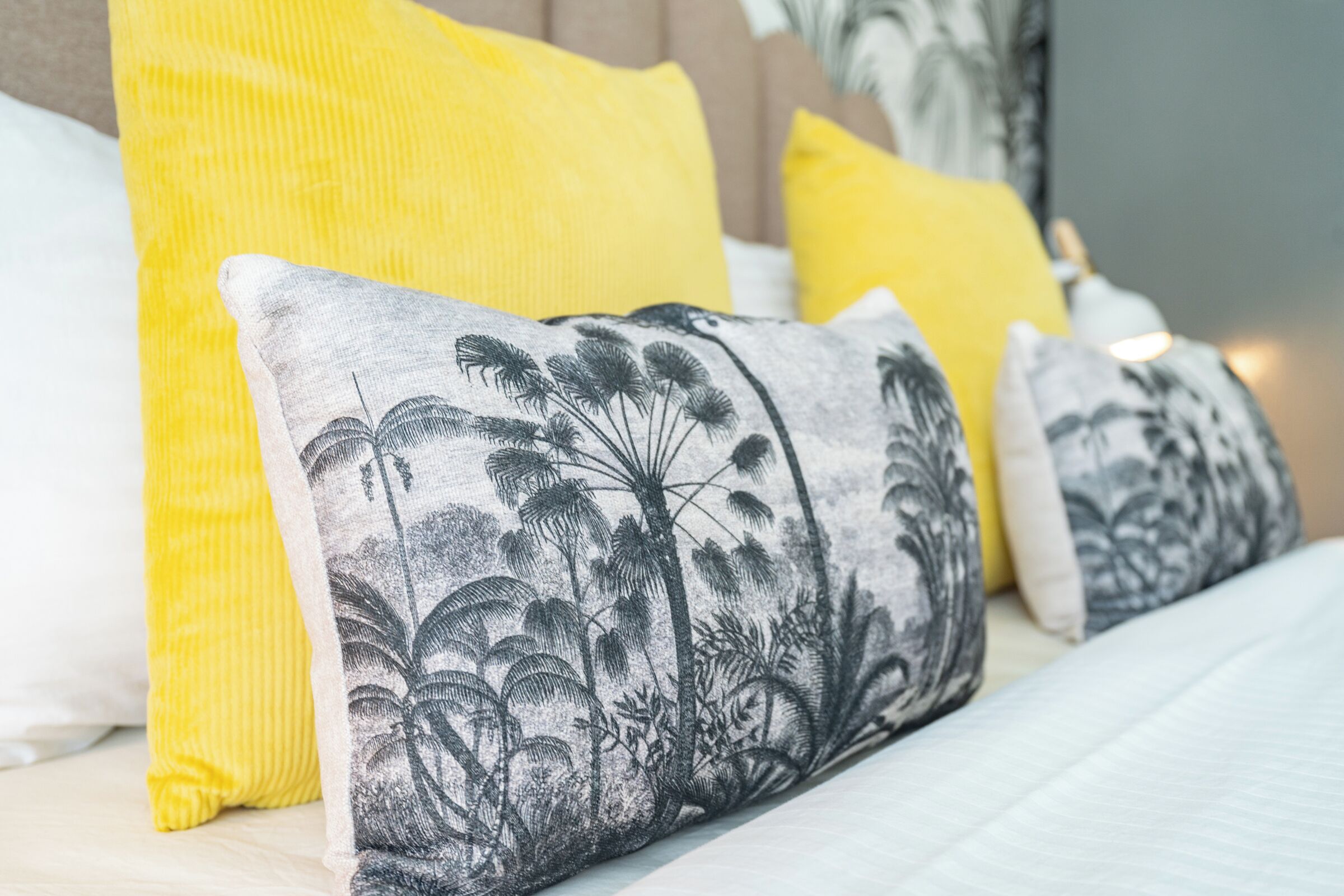 A bed with a white and gray patterned pillow and a yellow pillow.
