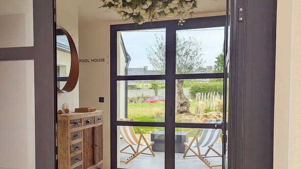 Ein Poolhaus-Eingang mit Glastür, einem Holzschrank mit Schubladen und zwei gestreiften Liegestühlen davor.