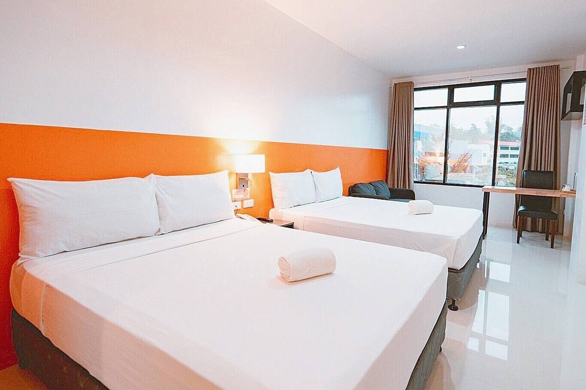 Une chambre d’hôtel avec deux lits, un bureau et une fenêtre avec des rideaux.