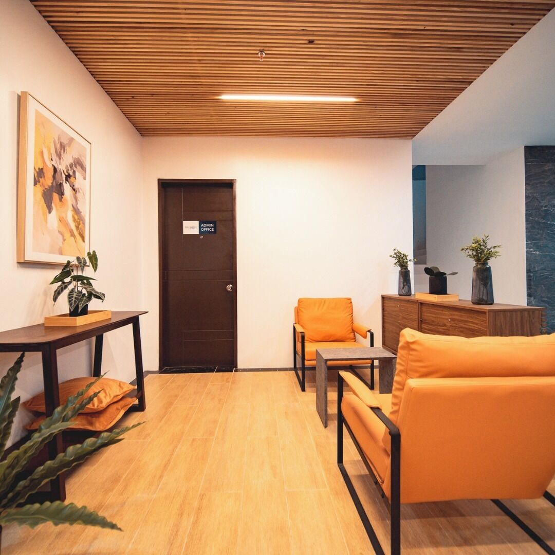 A modern waiting area with a wooden ceiling, a reception desk, an orange sofa, and a small table with plants.