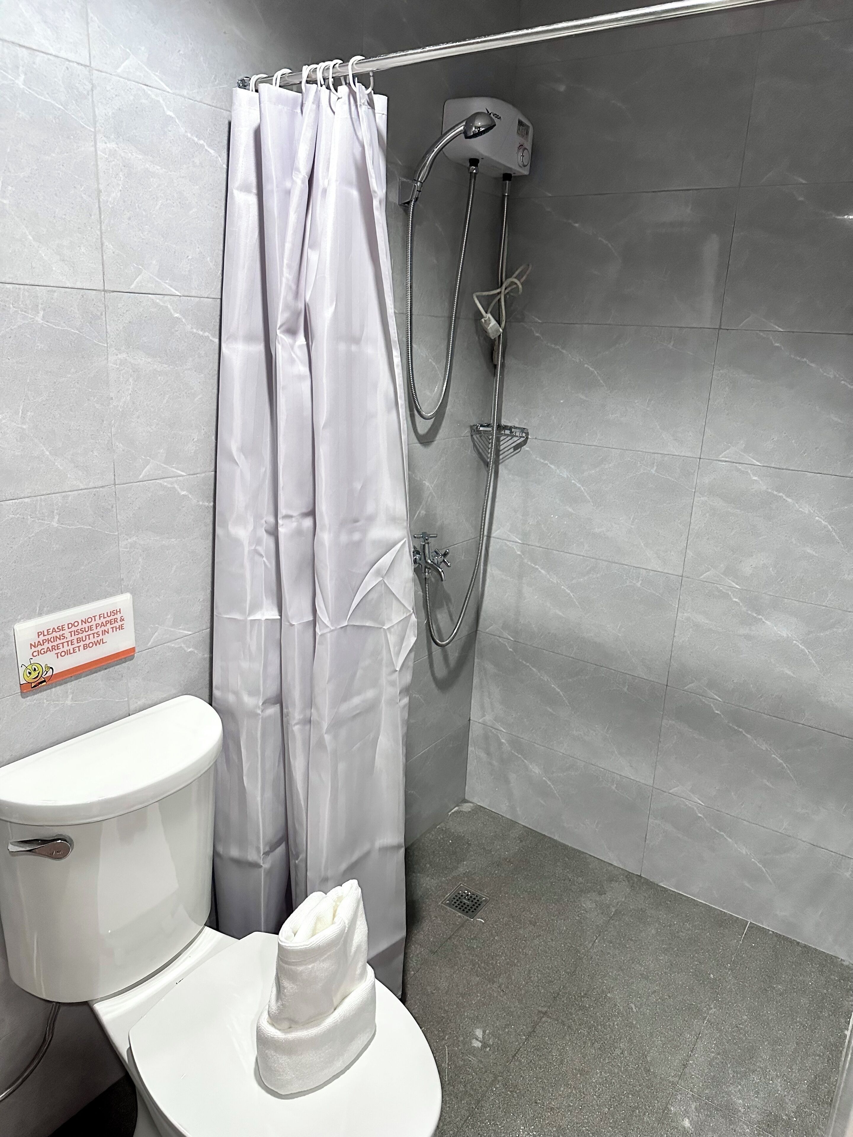 A bathroom with a toilet, shower, and a sign instructing not to flush napkins, tissue paper, or cigarette butts in the toilet bowl.