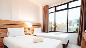 Ein Hotelzimmer mit zwei Betten, einem Holzkopfende, einem großen Fenster mit Vorhängen und Blick auf Gebäude.
