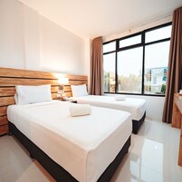 Habitación de hotel con dos camas, cabecero de madera, una ventana grande con cortinas y vistas a edificios.
