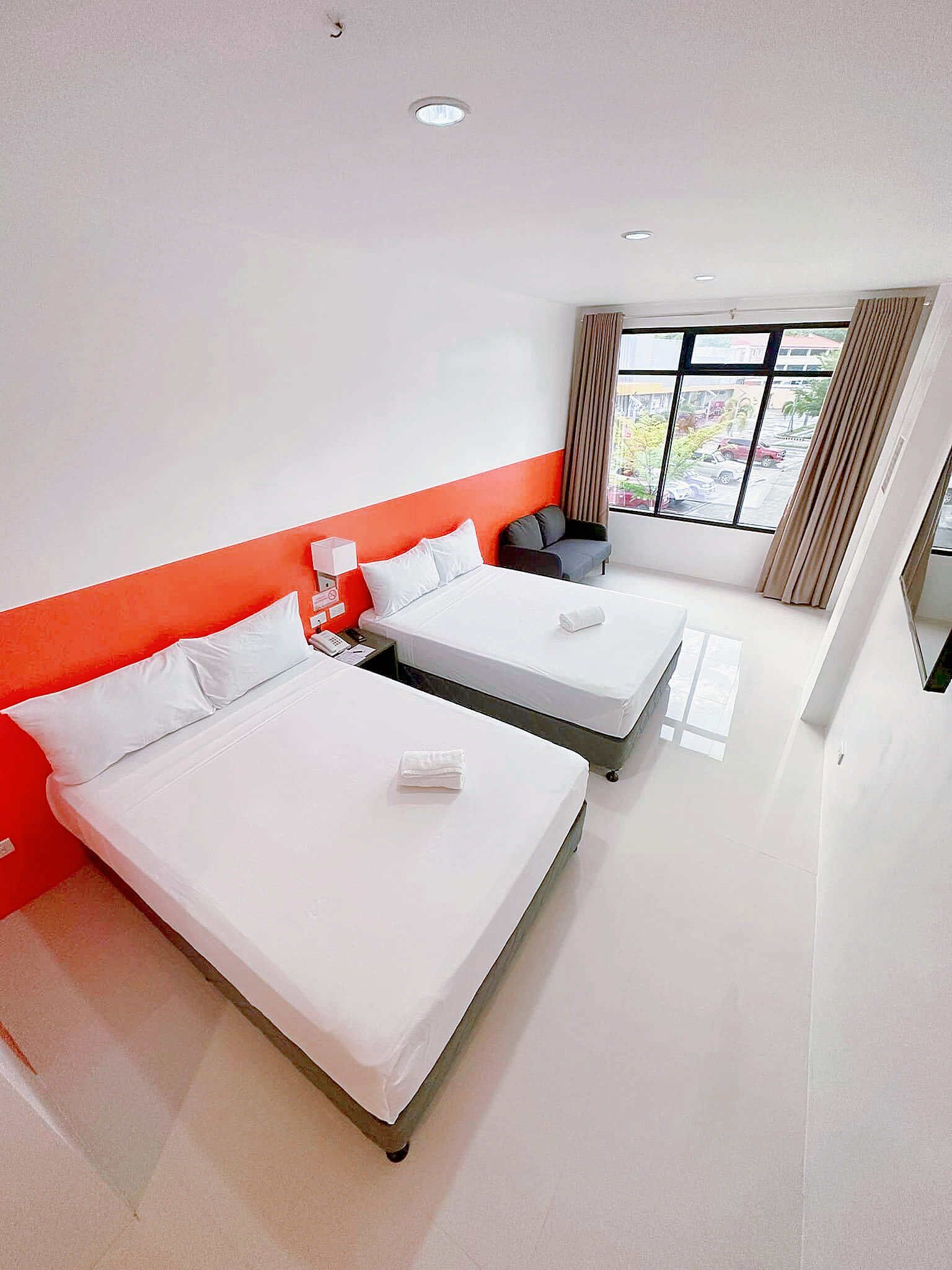 Ein Hotelzimmer mit zwei Betten, einem Fenster mit Vorhängen und Blick nach draußen.