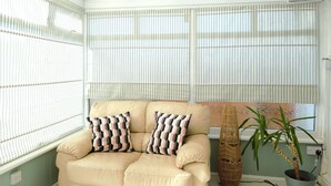 A room with a beige sofa, striped window blinds, a woven floor lamp, and a potted plant. - Family Seaside Bungalow - Max 6 Adults Only - 2 Small -Medium Sized Dogs Welcome - Nr Beach (Margate)