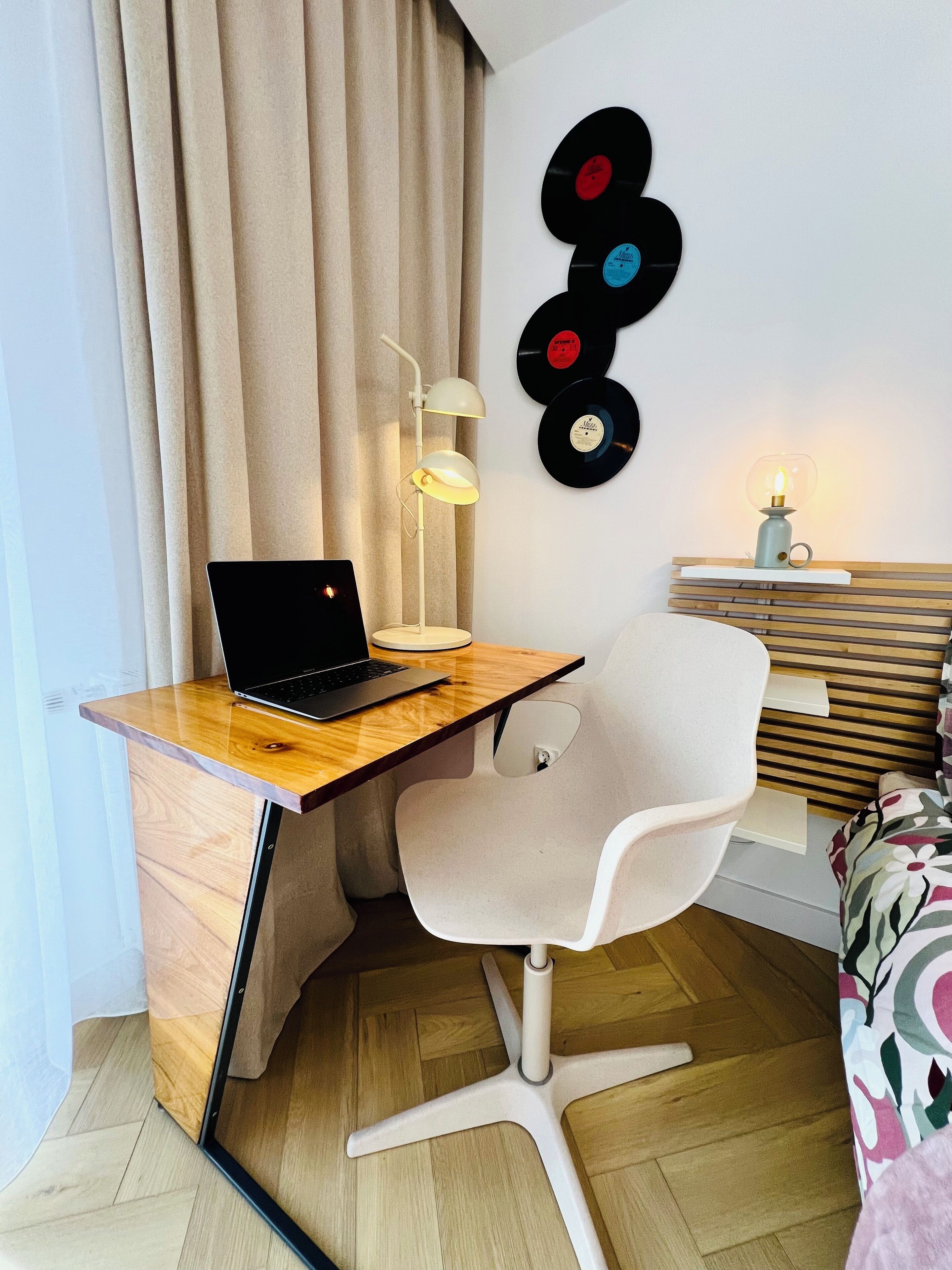A modern room with a wooden desk, a laptop, a white chair, a lamp, and a wall with vinyl records.