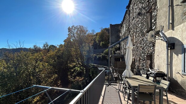 A terrace with a table and chairs, overlooking a scenic landscape with trees and a stone building. - Village house in the heart of Castagniccia (CARCHETO)