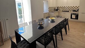 A modern kitchen with a checkered backsplash, a dining area with a long table and chairs, and pendant lighting. - Village house in the heart of Castagniccia (CARCHETO)
