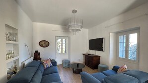 A living room with two blue sofas, a TV, a chandelier, and a window with a view. - Village house in the heart of Castagniccia (CARCHETO)
