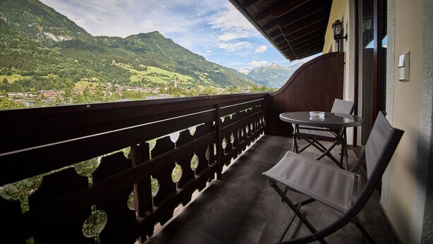A balcony with a view of a mountainous landscape, a table with a chair, and a small window. - Appartement Traumblick (Bad Hofgastein)