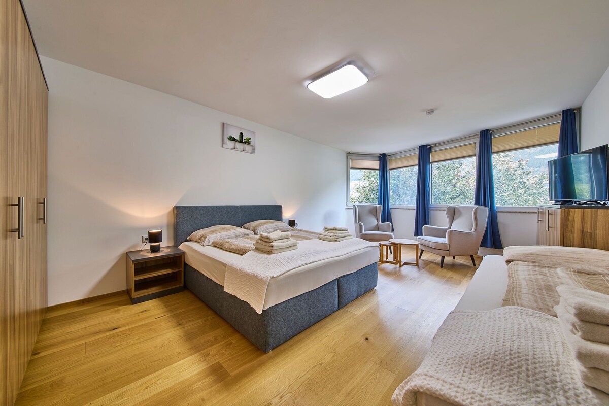 A modern bedroom with a large bed, bedside tables, a chair, and a TV.