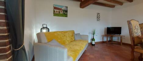 A living room with a sofa, a TV, a chair, and a painting on the wall.