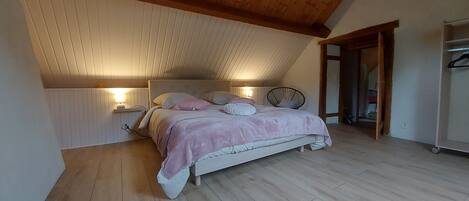 A bedroom with a sloped ceiling, a bed with a headboard, bedside lamps, and a wooden floor.