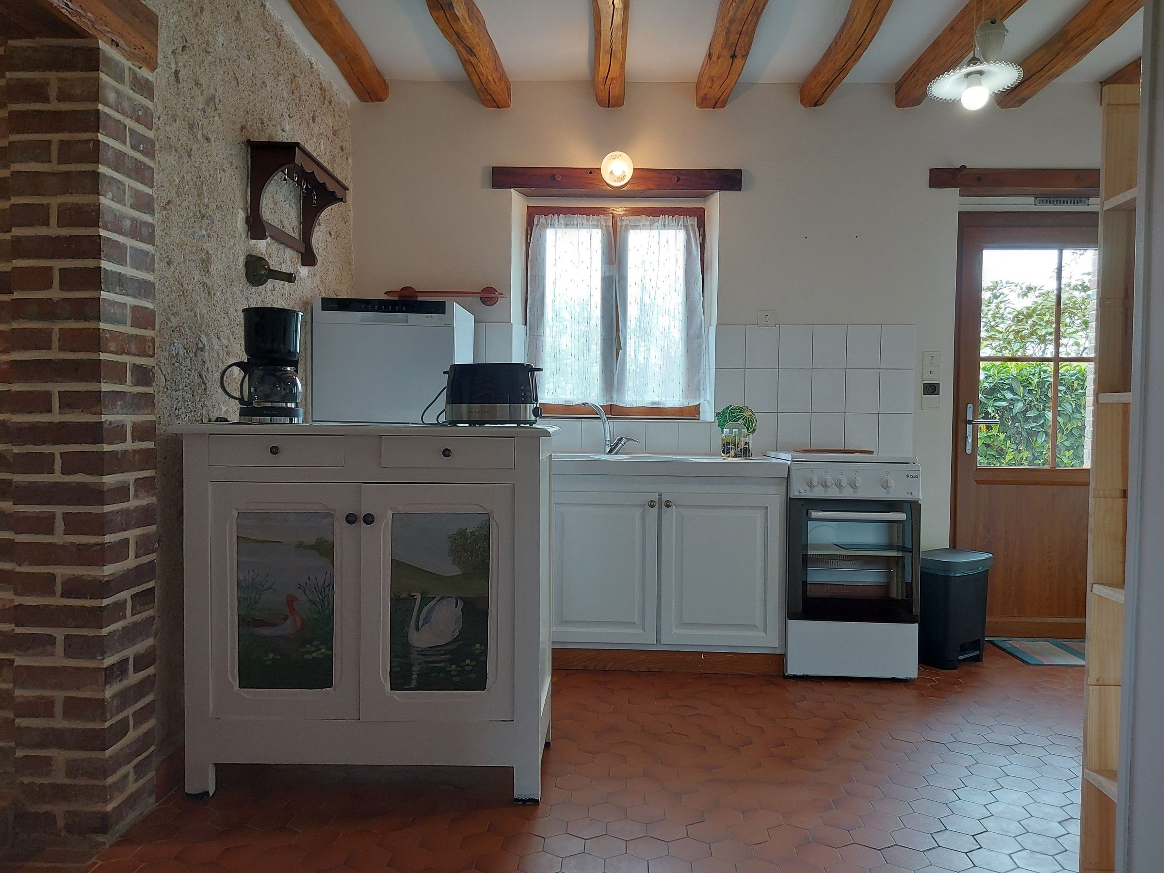 Une cuisine avec des meubles blancs, une cuisinière, un évier et une fenêtre avec des rideaux.