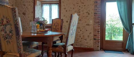 Un coin repas avec une table en bois, des chaises à motifs floraux et une vue par une fenêtre ornée de rideaux.