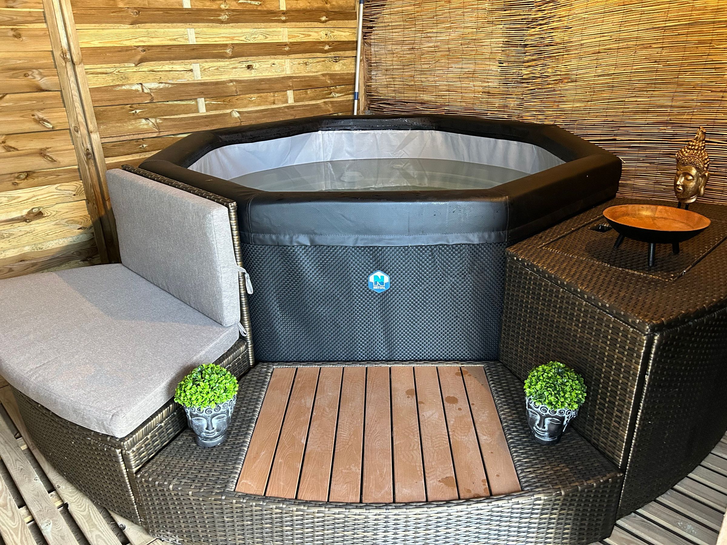Uma banheira de hidromassagem com área de estar, uma mesa de madeira e duas plantas em vasos.