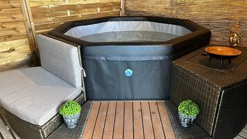 Uma banheira de hidromassagem com área de estar, uma mesa de madeira e duas plantas em vasos.