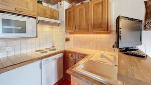 A compact kitchen with wooden cabinets, a microwave, a stove, a dishwasher, and a television. - 2-room apartment with parking, near the slopes (Combloux)