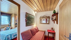A cozy room with a checkered sofa, a small bedside table with a mirror, and a window with curtains. - 2-room apartment with parking, near the slopes (Combloux)