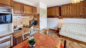 A kitchen with wooden cabinets, a microwave, a coffee maker, and a dining table with a floral tablecloth. - Cozy studio at the foot of the slopes with parking in Combloux (Combloux)