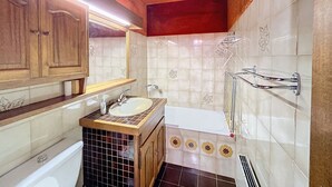 A bathroom with wooden cabinets, a sink, a mirror, a bathtub, and decorative tiles. - Cozy studio at the foot of the slopes with parking in Combloux (Combloux)