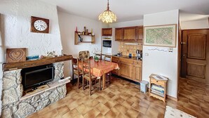 A kitchen with a stone fireplace, wooden cabinets, a dining table, and a hanging light fixture. - Cozy studio at the foot of the slopes with parking in Combloux (Combloux)