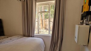 Een slaapkamer met een bed, gordijnen, een raam en een wandairconditioner.