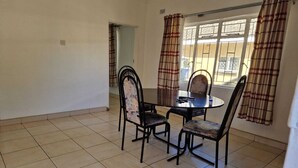 Een eetgedeelte met een ronde tafel en vier stoelen, een raam met gordijnen en een betegelde vloer.