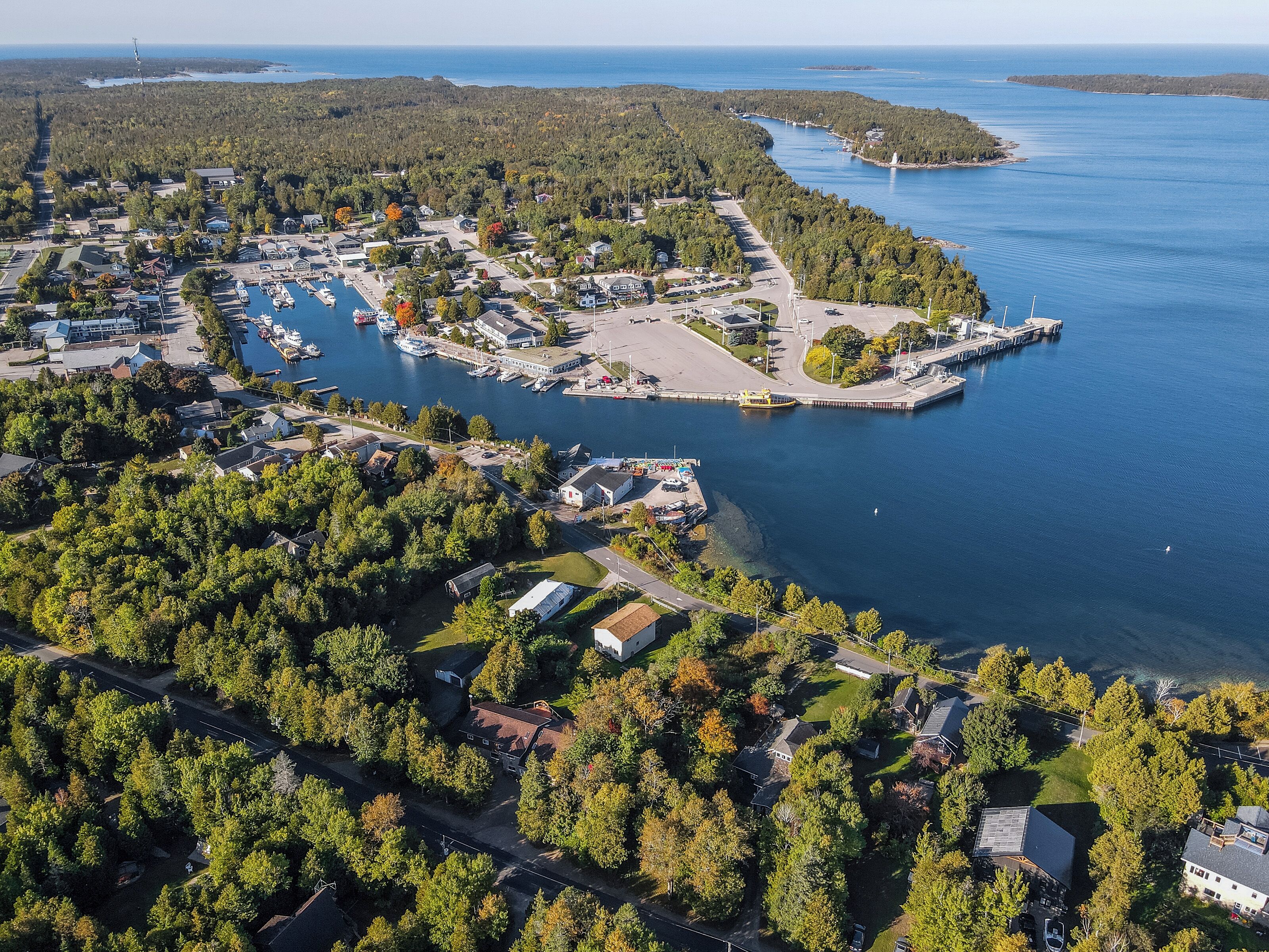 An aerial view of a coastal town with a marina, residential areas, and dense forest.