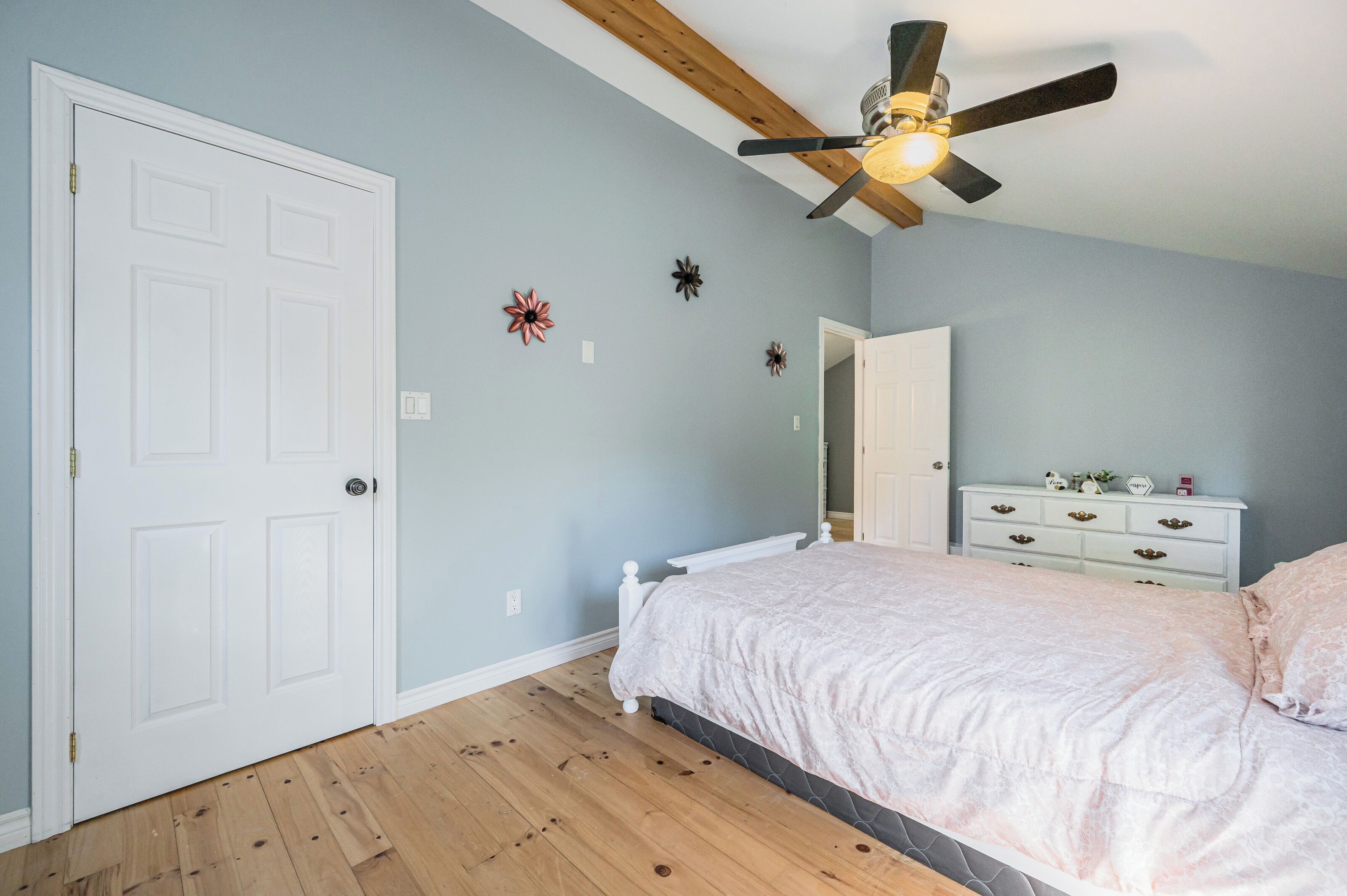 Camera da letto con letto, comò, ventilatore a soffitto e pavimento in legno.