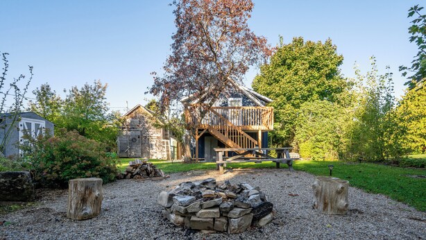 A rustic cabin with a wooden deck and a fire pit in the center.