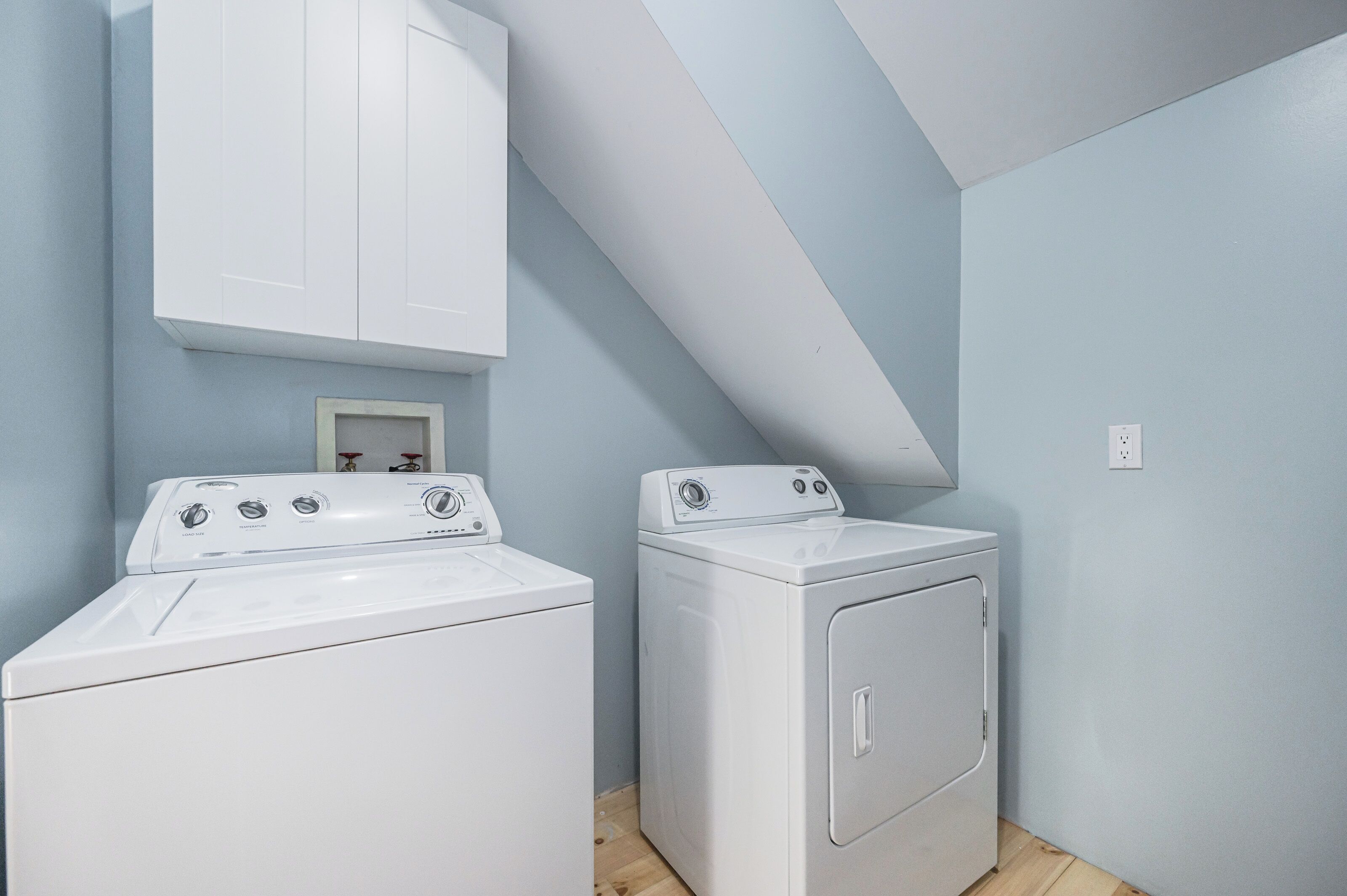 Een wasruimte met twee witte wasmachines, een wit kastje boven de linker machine, en een klein lijstwerk met een foto aan de muur.
