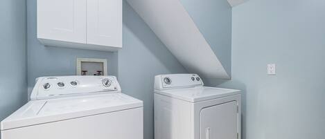Een wasruimte met twee witte wasmachines, een wit kastje boven de linker machine, en een klein lijstwerk met een foto aan de muur.