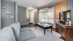 A living room with a gray sofa, a wooden cabinet with a TV, and a window with curtains.