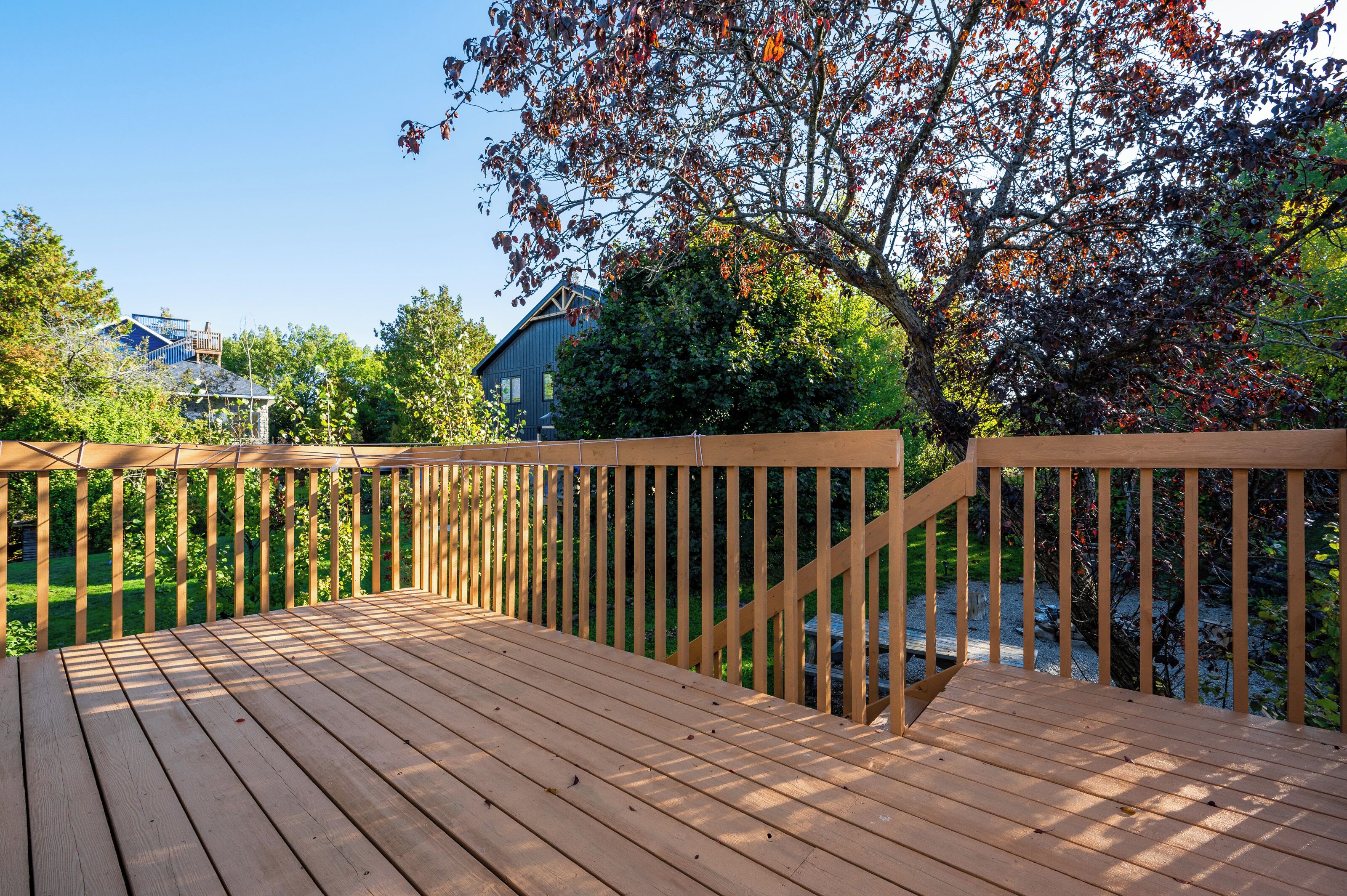 A wooden deck with a railing, surrounded by trees and a house in the background.