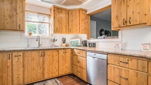 A kitchen with wooden cabinets, a dishwasher, and a window with blinds.