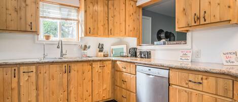 A kitchen with wooden cabinets, a dishwasher, and a window with blinds.
