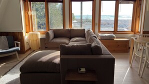 Una sala de estar acogedora con un sofá modular, una mesita y un rincón con ventanales que dan a un paisaje nevado.