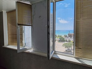 Une pièce dotée d’une grande fenêtre, de stores entrouverts et offrant une vue sur le paysage urbain.